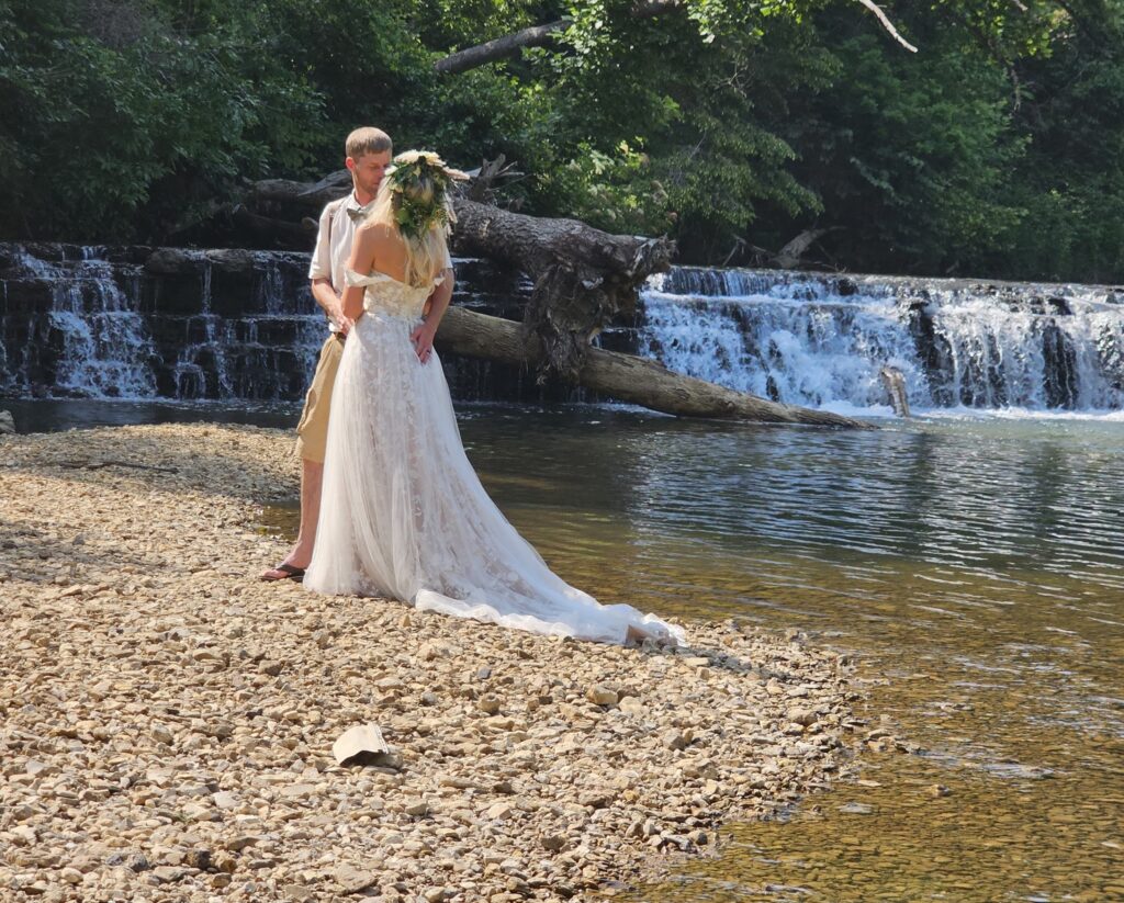 A picturesque scene of a bride and groom embracing beside a beautiful waterfall.